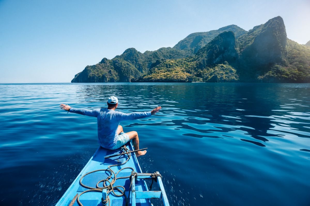 Traveler on a boat with arms outstretched, sailing through the islands of Palawan